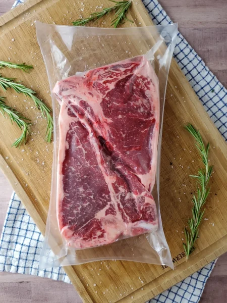 Vacuum-sealed ribeye steak on a wooden cutting board, surrounded by fresh rosemary sprigs and coarse sea salt, ideal for grilling or sous vide cooking.